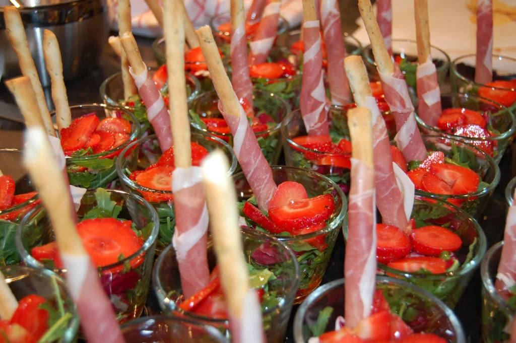 Kleine Gläser mit Grissini, Schinken, Erdbeeren und Rucola, festlich arrangiert für ein Buffet.