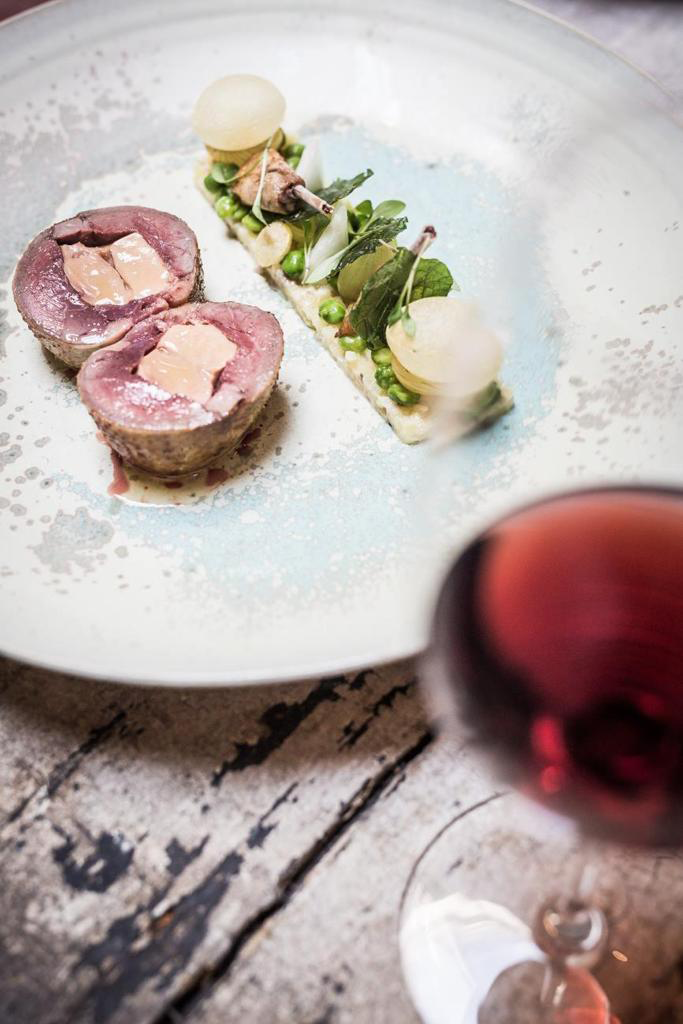 Ein elegant angerichtetes Fleischgericht mit Gemüse und einem Glas roséfarbenem Wein auf einem Holztisch.