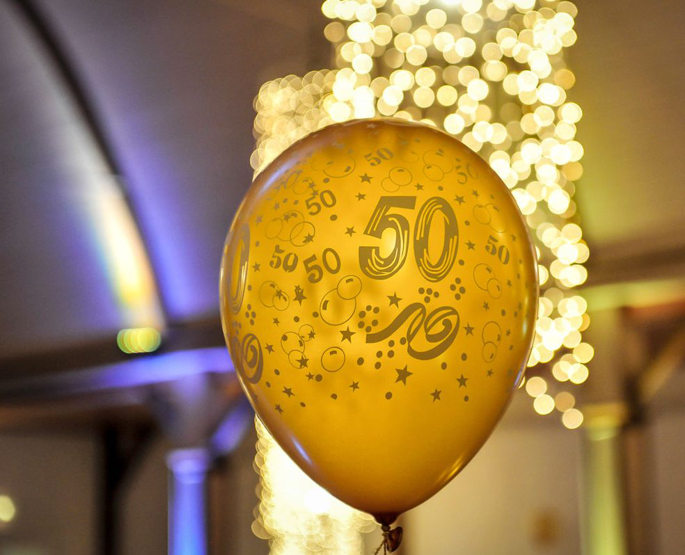 Goldener Ballon mit "50", umgeben von verschwommenen Lichtern, schafft festliche Stimmung.
